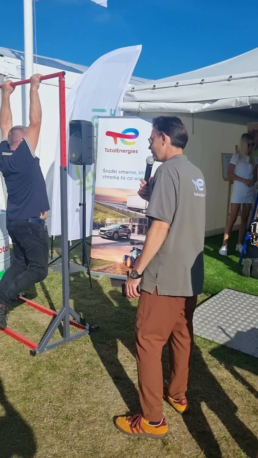 Prowadzący z mikrofonem przy konkursie podciągania na drążku na stoisku TotalEnergies podczas Agro Show