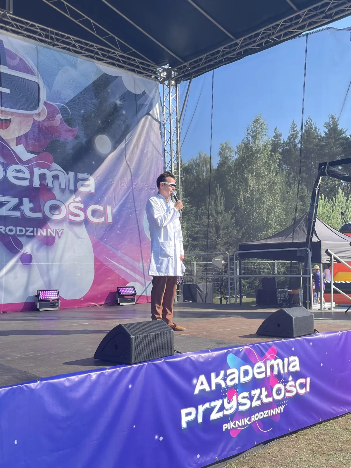 Prowadzący z mikrofonem na scenie pikniku rodzinnego Akademia Przyszłości Sieci Badawczej Łukasiewicz