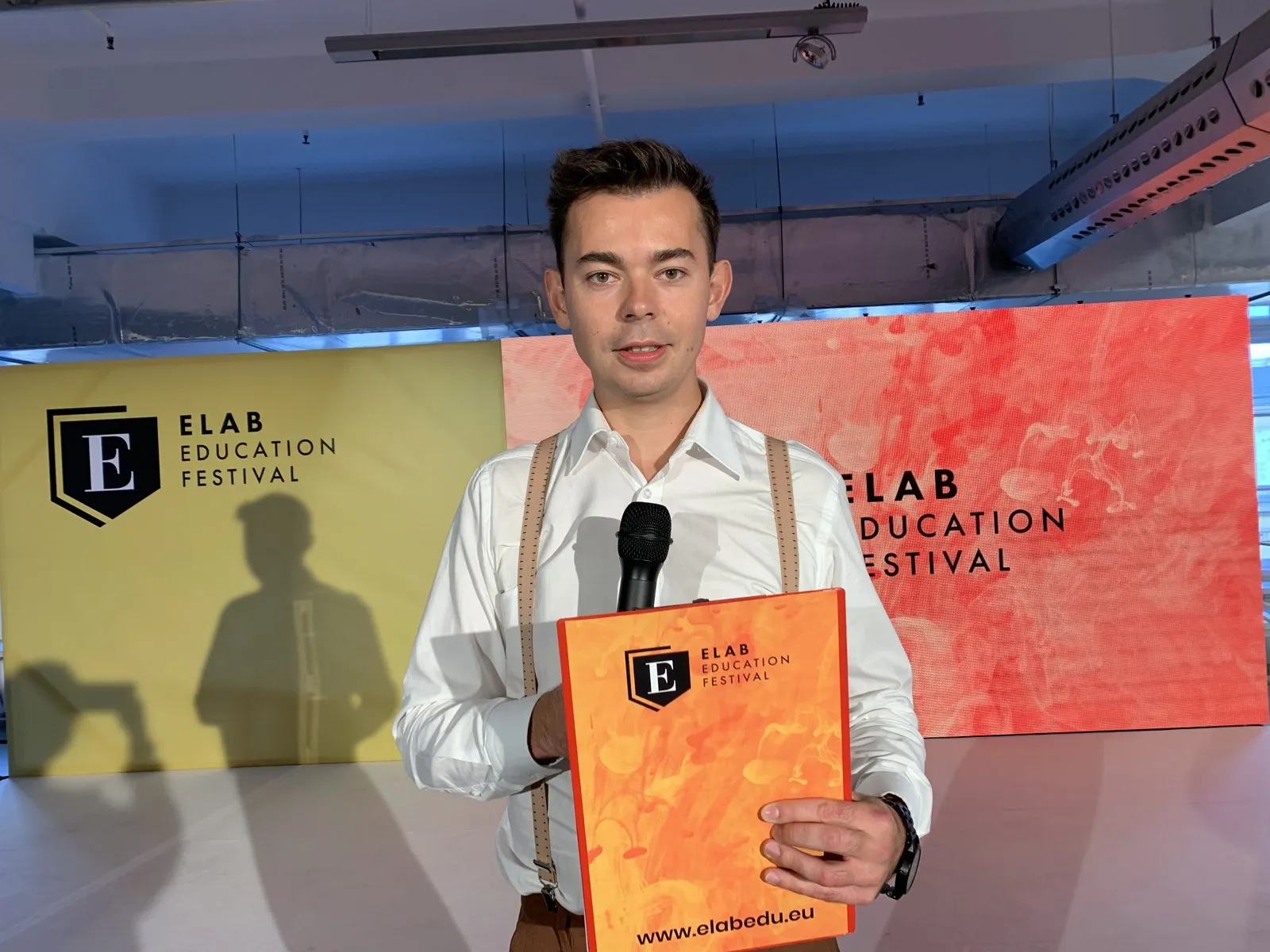 Konferansjer Szymon Alaba z mikrofonem i scenariuszem na scenie Elab Education Festival 2019 w Warszawie