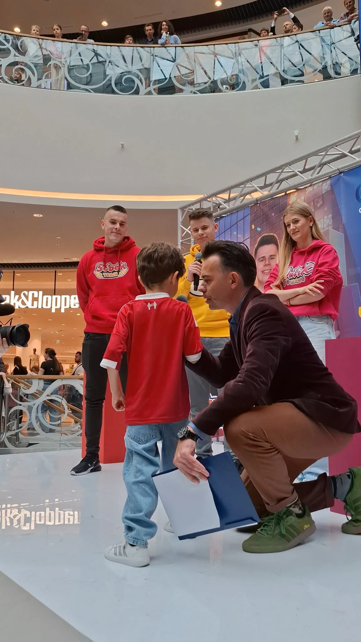 Konferansjer Szymon Alaba przykucnięty przy małym fanie na scenie spotkania ze SmileSlow w G City Promenada
