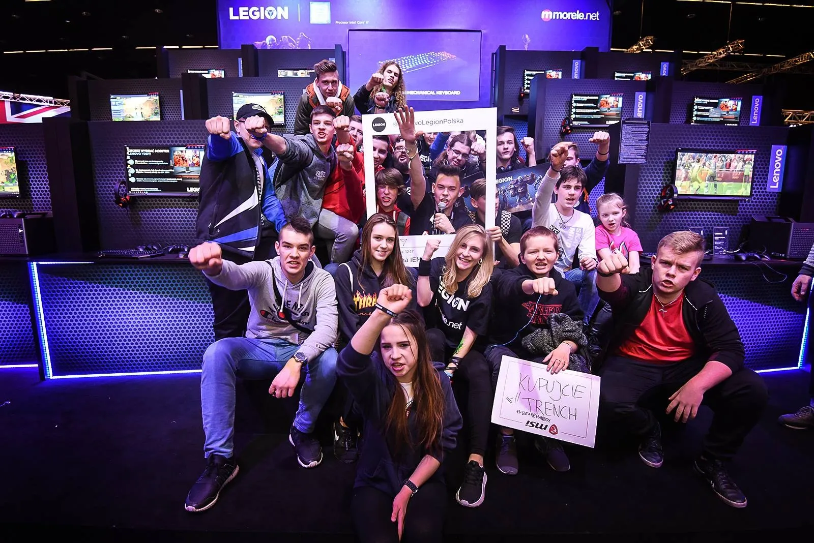 Szymon Alaba z mikrofonem wśród uczestników konkursu w strefie Lenovo Legion, zdjęcie grupowe w ramce marki