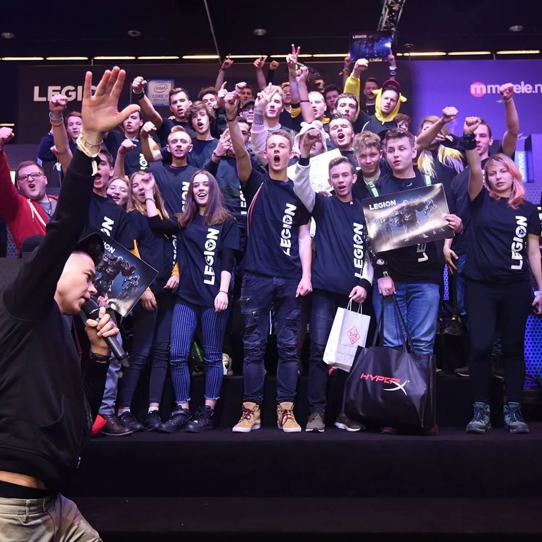 Szymon Alaba z mikrofonem przed grupą uczestników w koszulkach Legion na scenie strefy Lenovo