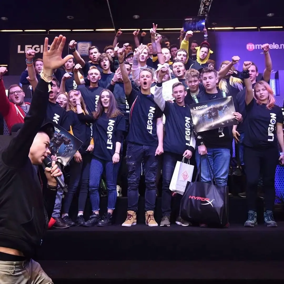 Prowadzący z mikrofonem przed grupą graczy w koszulkach Legion podczas IEM Katowice