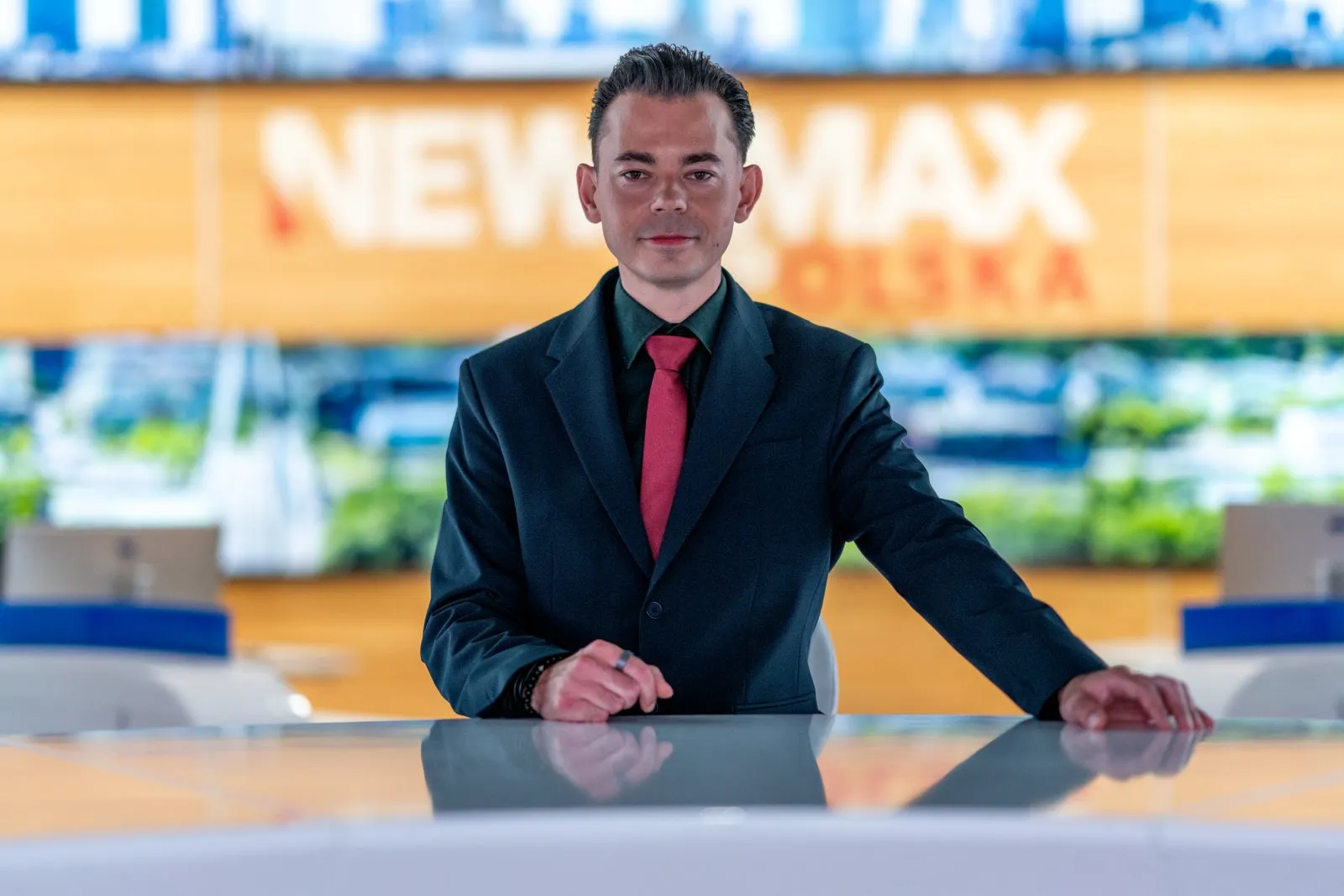 Szymon Alaba przy stole prezenterskim w studiu Newsmax Polska TV