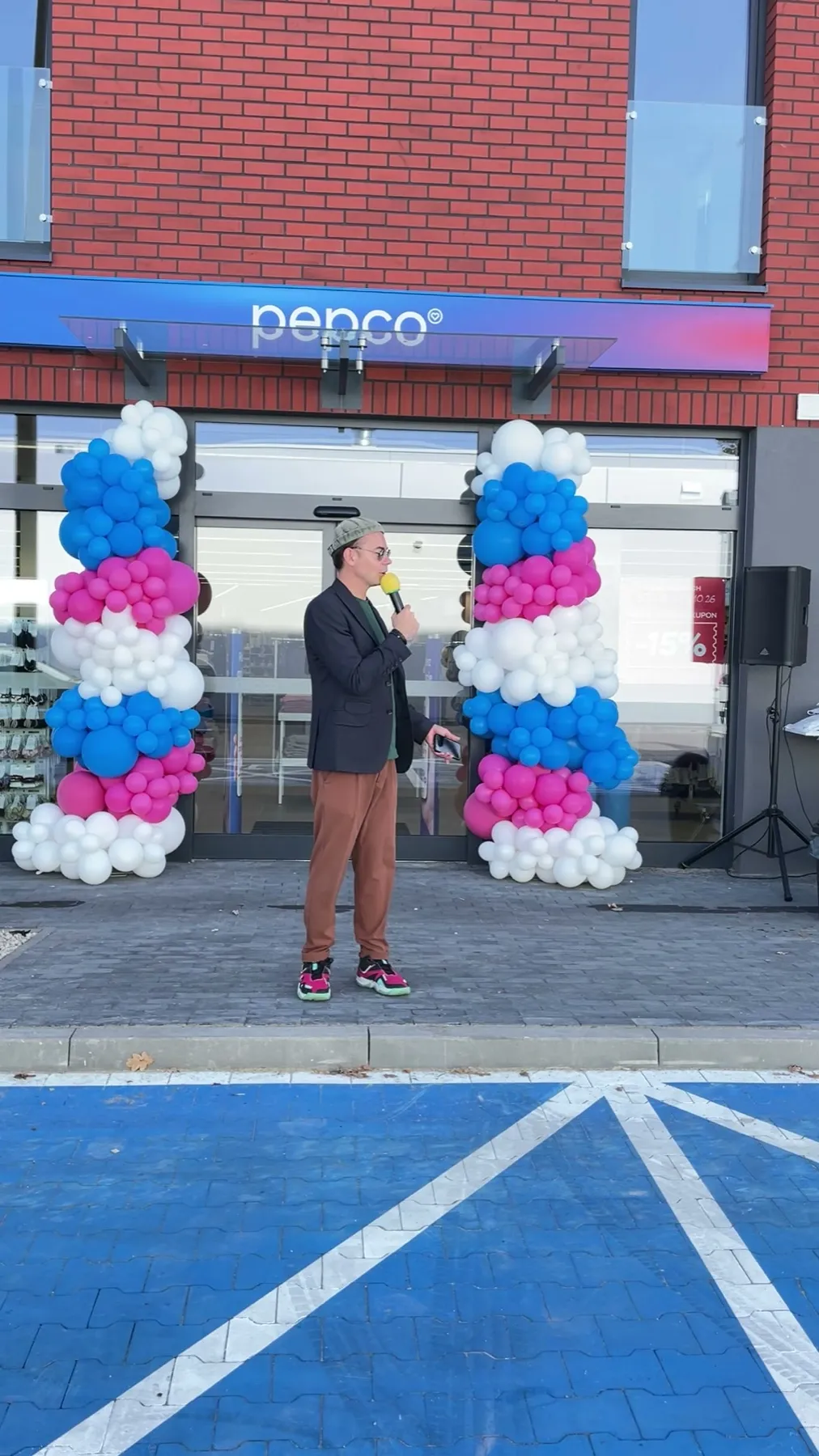 Konferansjer Szymon Alaba z mikrofonem między balonowymi kolumnami przed nowym sklepem Pepco przy ul. Rudzkiej w Łodzi