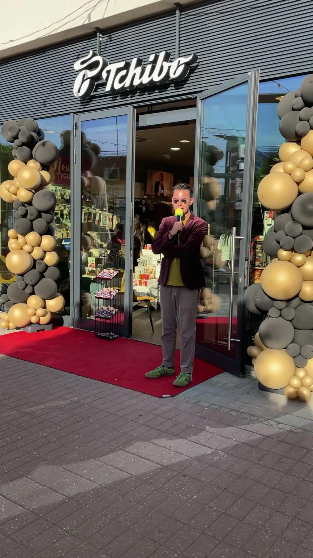 Prowadzący z mikrofonem przed wejściem do Tchibo w Gdańsku między balonowymi kolumnami w kolorach czarnym i złotym