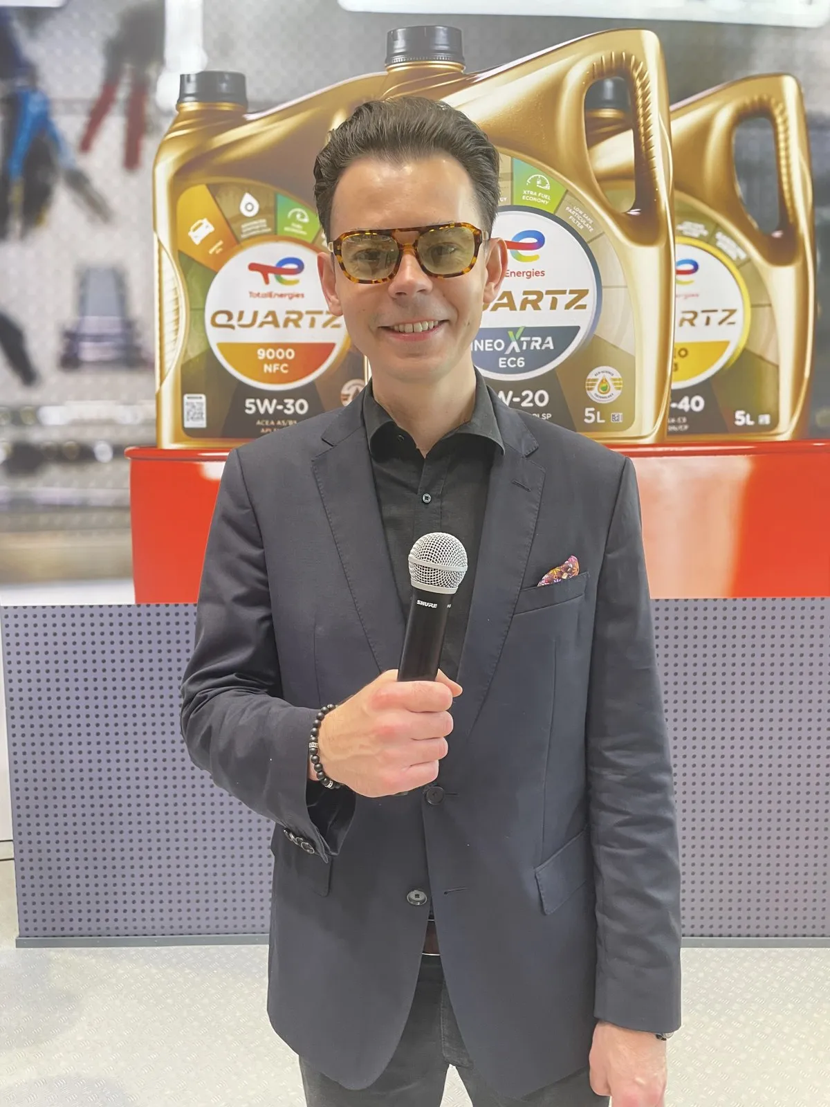 Konferansjer Szymon Alaba z mikrofonem na stoisku TotalEnergies przed ekspozycją olejów Quartz na Poznań Motor Show 2026