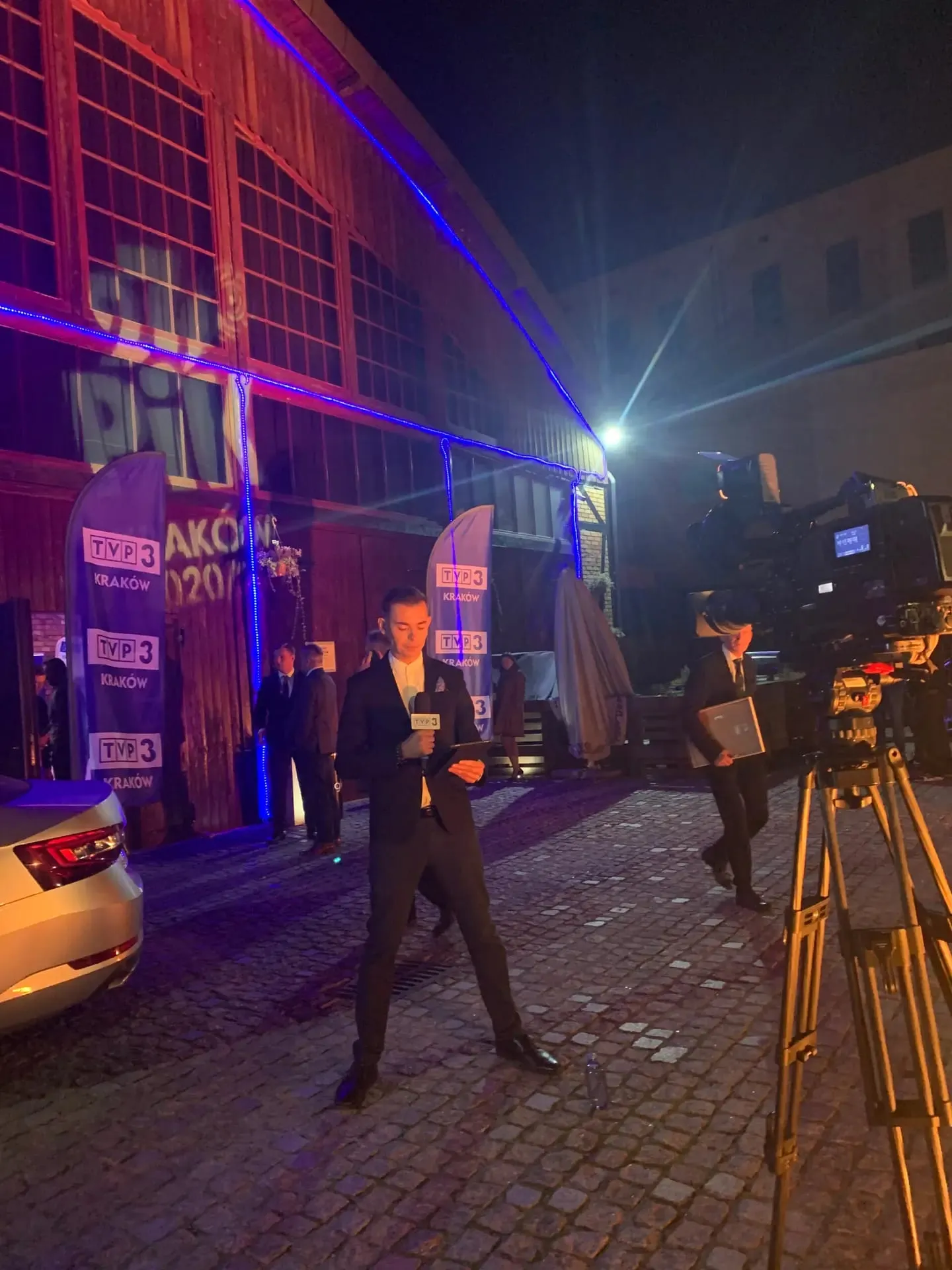 Prowadzący w garniturze z mikrofonem wieczorem przy kamerze podczas Przeglądu Oddziałów Terenowych TVP w Krakowie
