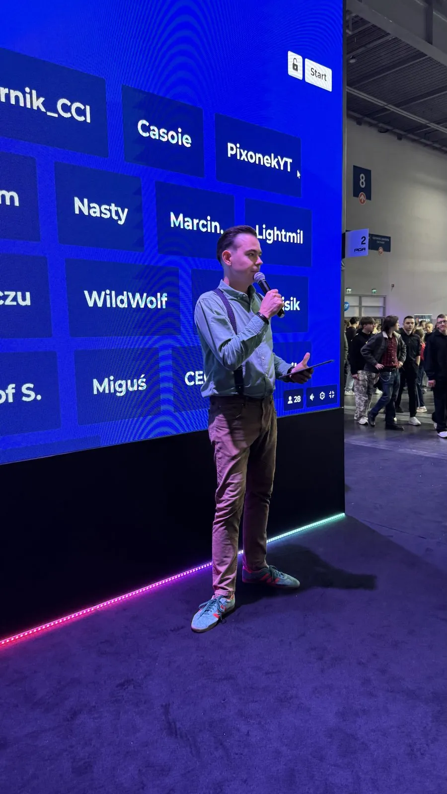 Szymon Alaba prowadzi quiz Kahoot na scenie strefy x-kom, za nim ekran z nazwami graczy