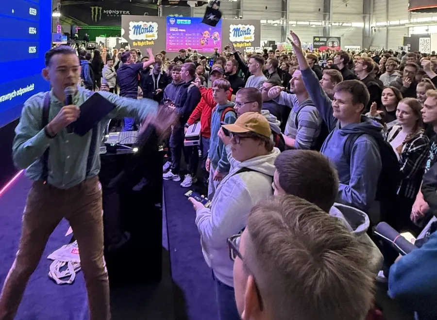Konferansjer Szymon Alaba z mikrofonem przed tłumem graczy na scenie x-kom podczas Poznań Game Arena 2025