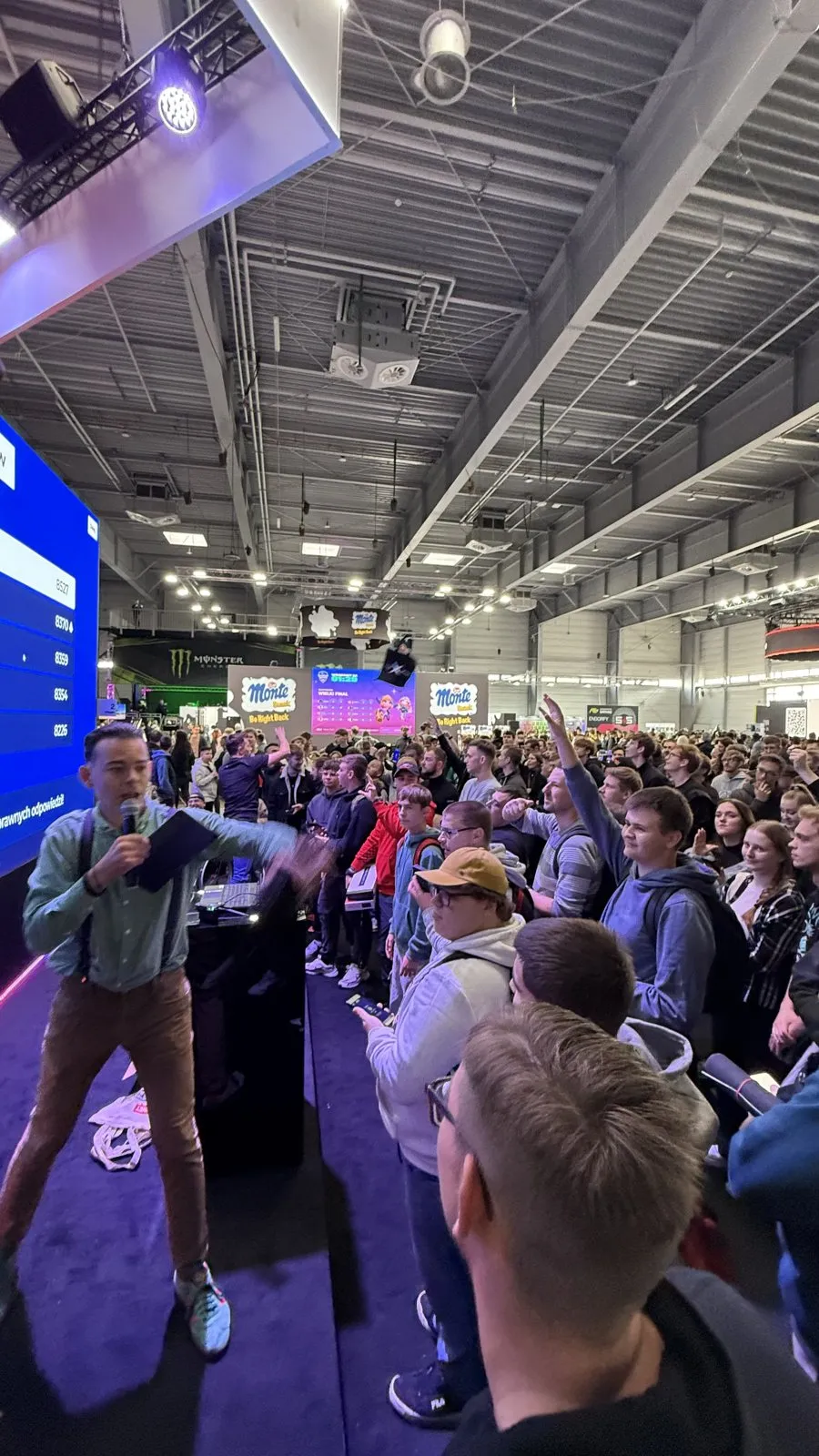 Konferansjer z mikrofonem przed tłumem graczy na scenie x-kom podczas Poznań Game Arena 2025